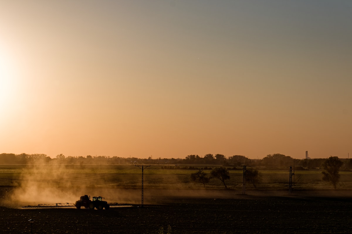 Traktor mit Anbaugerät bei der Feldarbeit im Abendlicht